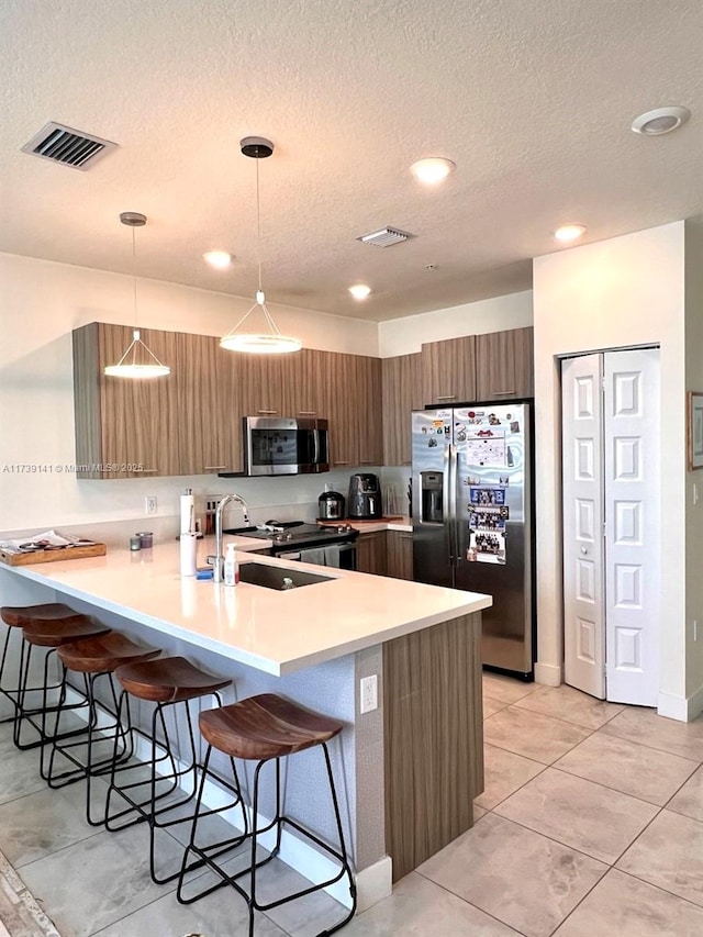 kitchen with sink, stainless steel appliances, a kitchen bar, decorative light fixtures, and kitchen peninsula