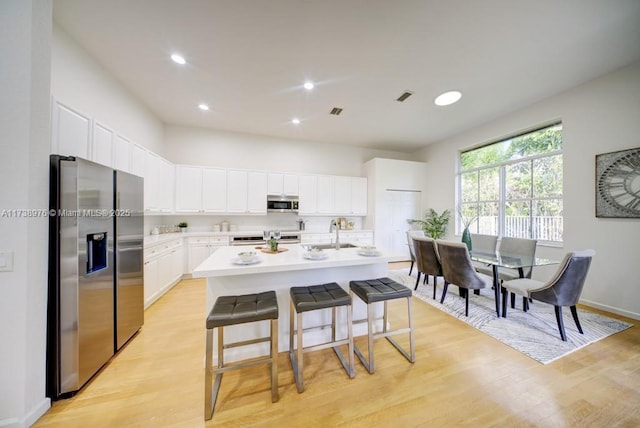 kitchen featuring white cabinets, a kitchen bar, a kitchen island with sink, stainless steel appliances, and light hardwood / wood-style flooring