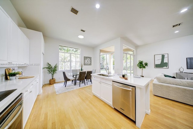 kitchen with appliances with stainless steel finishes, white cabinetry, an island with sink, sink, and light hardwood / wood-style flooring