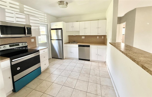 kitchen with light tile patterned floors, sink, stainless steel appliances, tasteful backsplash, and white cabinets