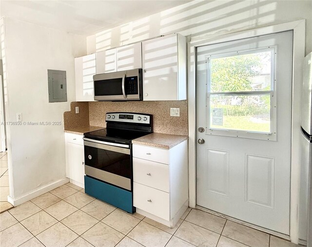 kitchen with light tile patterned floors, appliances with stainless steel finishes, electric panel, decorative backsplash, and white cabinets