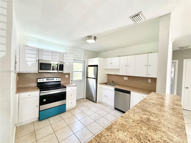 kitchen with sink, white cabinets, backsplash, light tile patterned floors, and stainless steel appliances