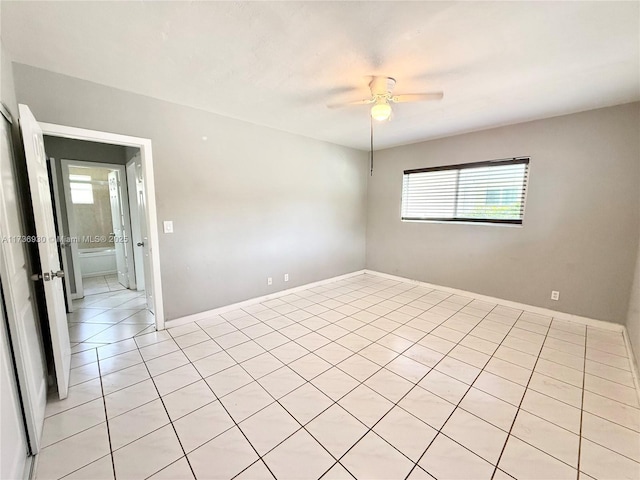 empty room featuring ceiling fan, light tile patterned floors, and baseboards