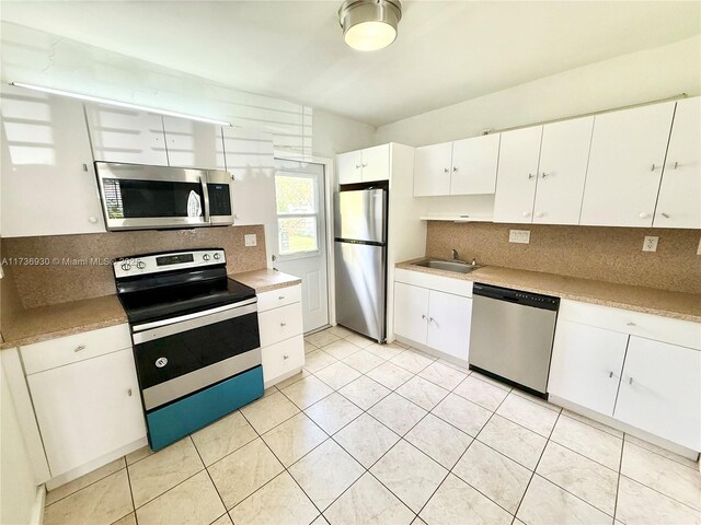 kitchen featuring light tile patterned floors, sink, appliances with stainless steel finishes, white cabinetry, and backsplash