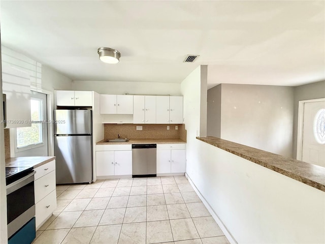 kitchen featuring sink, light tile patterned floors, appliances with stainless steel finishes, white cabinetry, and decorative backsplash