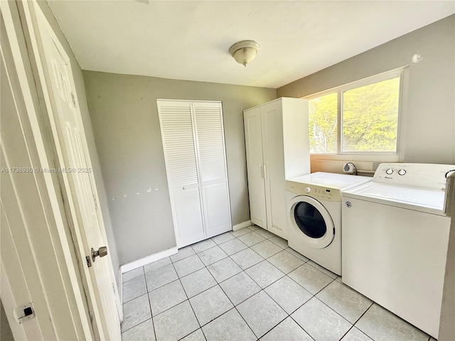 clothes washing area featuring washer and clothes dryer, light tile patterned flooring, cabinet space, and baseboards