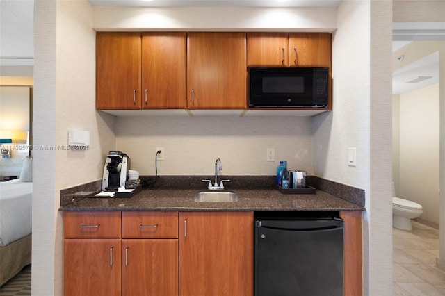 kitchen featuring dark stone counters, refrigerator, sink, and black microwave