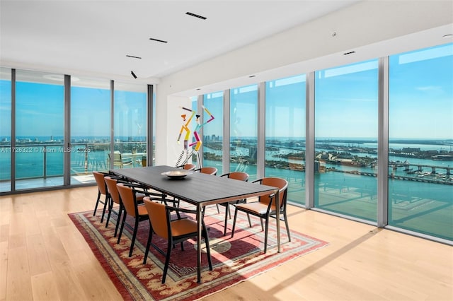 dining space featuring a water view, a wall of windows, and light hardwood / wood-style flooring