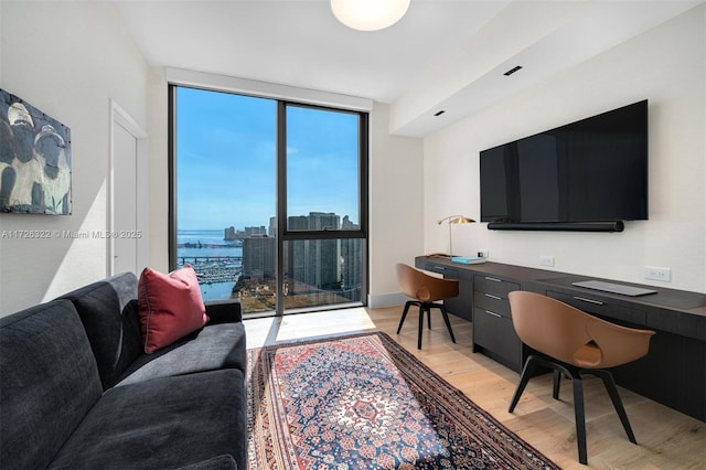 office area with floor to ceiling windows, built in desk, and light hardwood / wood-style flooring