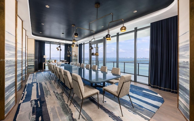 dining room featuring a water view, floor to ceiling windows, a raised ceiling, and hardwood / wood-style floors