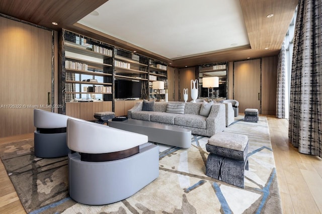 living room featuring built in shelves, wood walls, wood ceiling, light wood-type flooring, and a raised ceiling