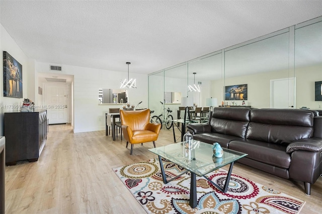 living room featuring a textured ceiling, a chandelier, and light wood-type flooring