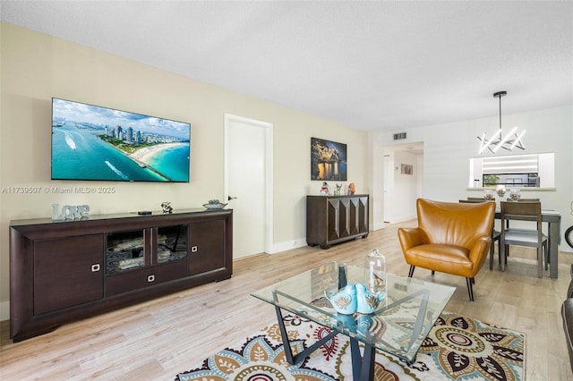 living room featuring a chandelier, a textured ceiling, and light wood-type flooring