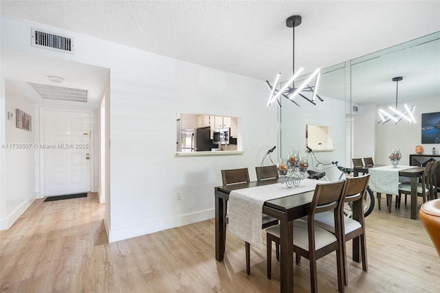 dining area featuring light wood-type flooring, a textured ceiling, and an inviting chandelier