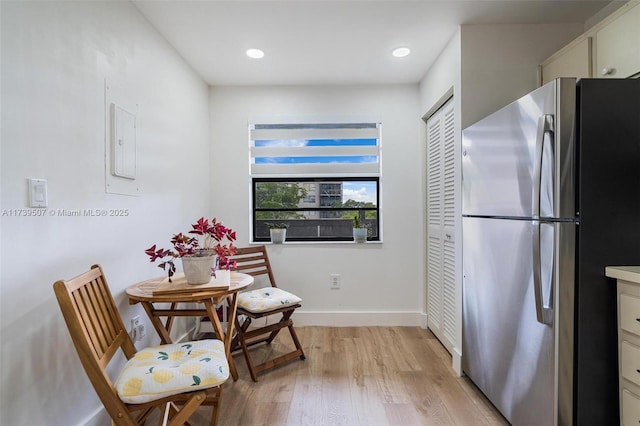 kitchen featuring white cabinetry, light wood-type flooring, electric panel, and stainless steel refrigerator