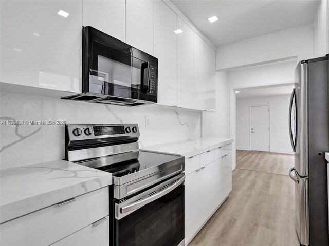 kitchen featuring light hardwood / wood-style flooring, stainless steel appliances, light stone countertops, decorative backsplash, and white cabinets