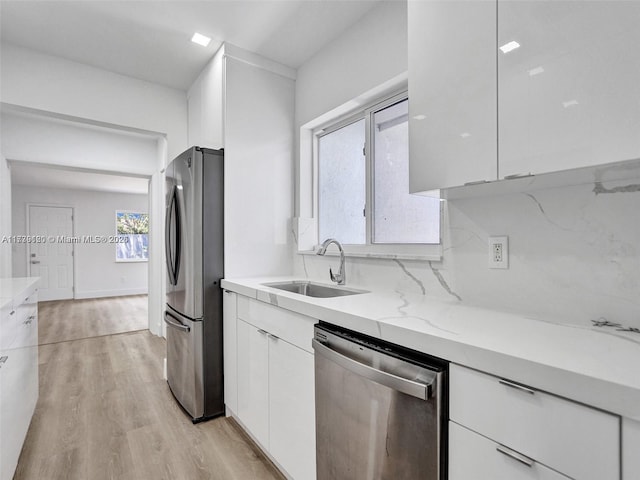 kitchen featuring appliances with stainless steel finishes, sink, white cabinets, light stone counters, and light wood-type flooring