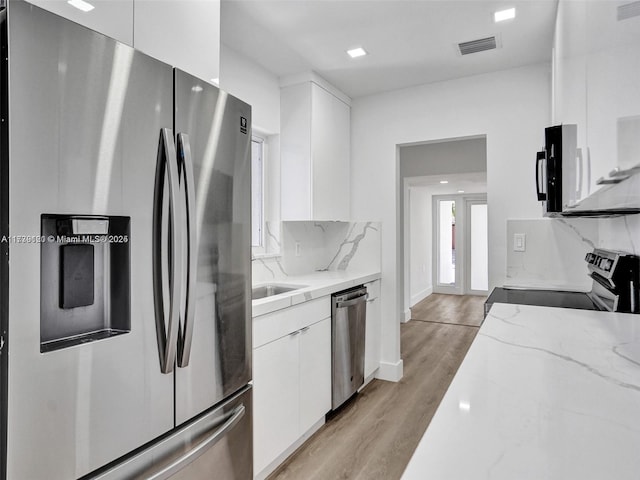 kitchen with white cabinets, decorative backsplash, stainless steel appliances, light stone countertops, and light wood-type flooring