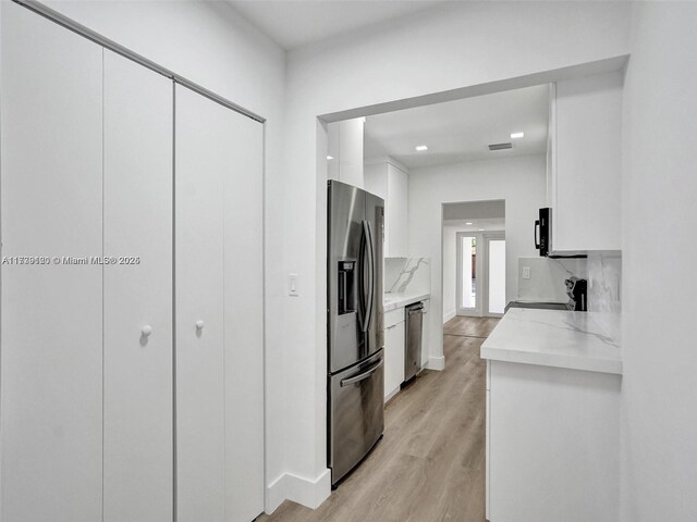 kitchen featuring white cabinetry, decorative backsplash, stainless steel appliances, and light hardwood / wood-style floors