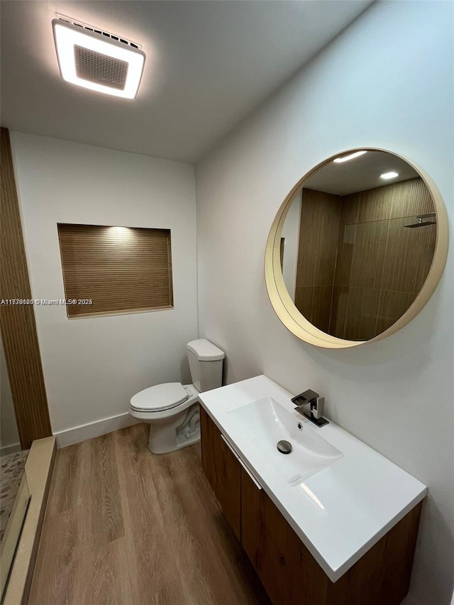 bathroom featuring wood-type flooring, toilet, vanity, and a shower