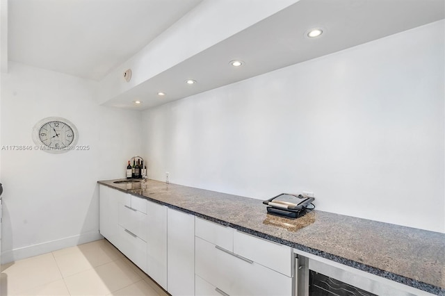 kitchen featuring sink, dark stone countertops, light tile patterned floors, beverage cooler, and white cabinets