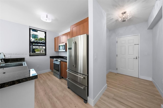 kitchen with sink, appliances with stainless steel finishes, dark stone countertops, light hardwood / wood-style floors, and a chandelier