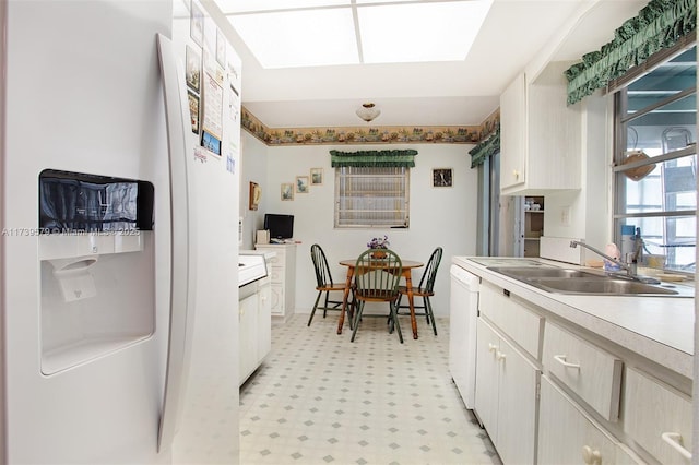 kitchen featuring white dishwasher, sink, and a skylight