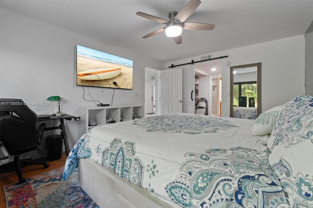 bedroom with ceiling fan, wood-type flooring, and a barn door