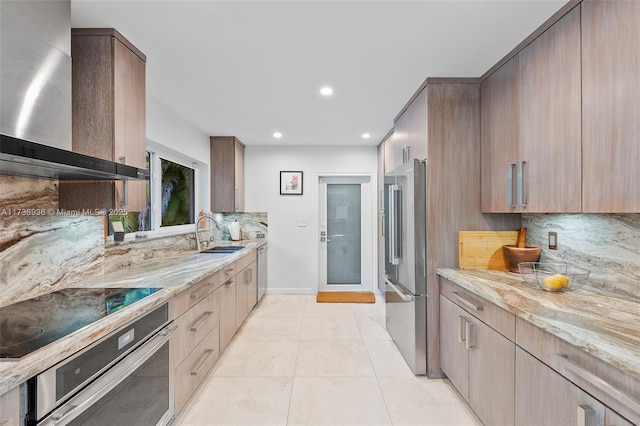 kitchen with sink, wall chimney range hood, stainless steel appliances, light stone countertops, and backsplash