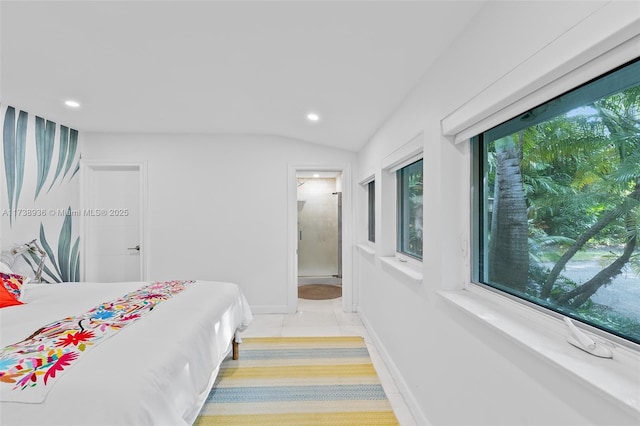 bedroom with lofted ceiling, light tile patterned floors, and ensuite bath