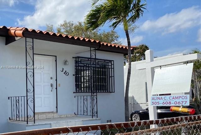 property entrance with a tiled roof, fence, and stucco siding