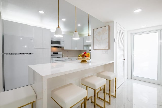 kitchen with hanging light fixtures, a breakfast bar, white cabinets, and white appliances