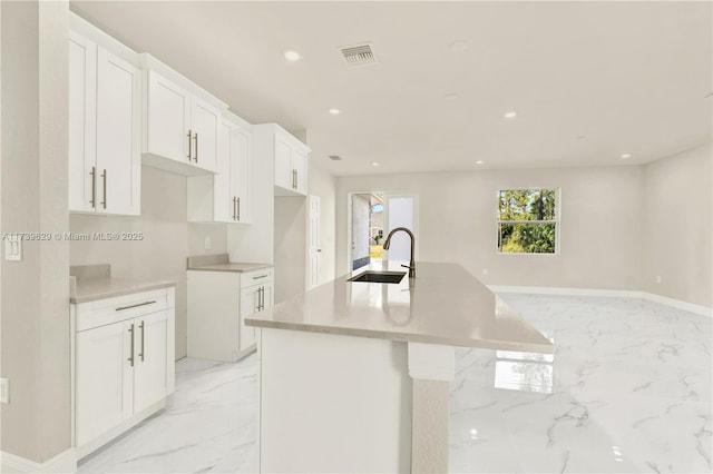 kitchen featuring an island with sink, sink, and white cabinets