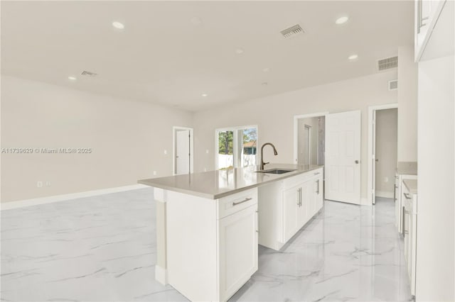 kitchen with a kitchen island with sink, sink, and white cabinets