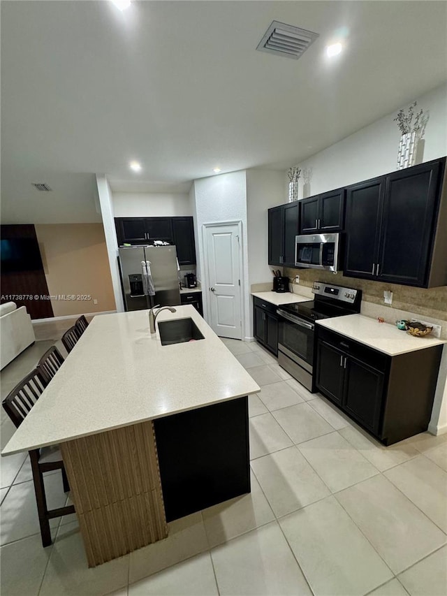 kitchen with an island with sink, sink, a kitchen breakfast bar, decorative backsplash, and stainless steel appliances