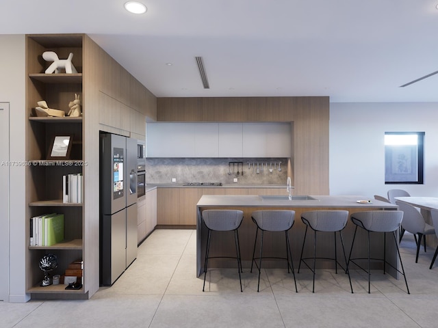 kitchen featuring a breakfast bar, stainless steel appliances, an island with sink, and light brown cabinets