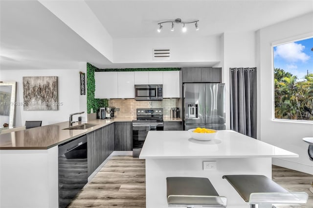 kitchen featuring stainless steel appliances, a kitchen bar, kitchen peninsula, and white cabinets