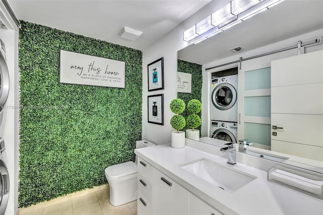 bathroom featuring tile patterned flooring, vanity, stacked washer / drying machine, and toilet