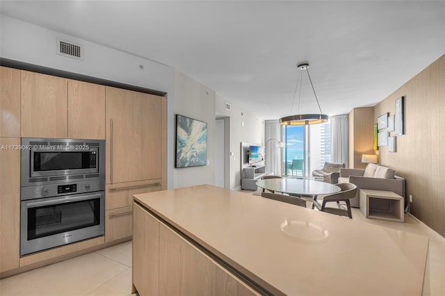 kitchen with light tile patterned floors, decorative light fixtures, light brown cabinets, and appliances with stainless steel finishes