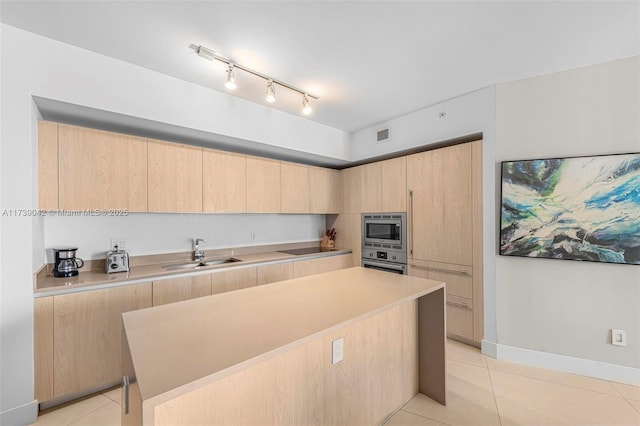 kitchen with light tile patterned flooring, light brown cabinetry, sink, appliances with stainless steel finishes, and a kitchen island