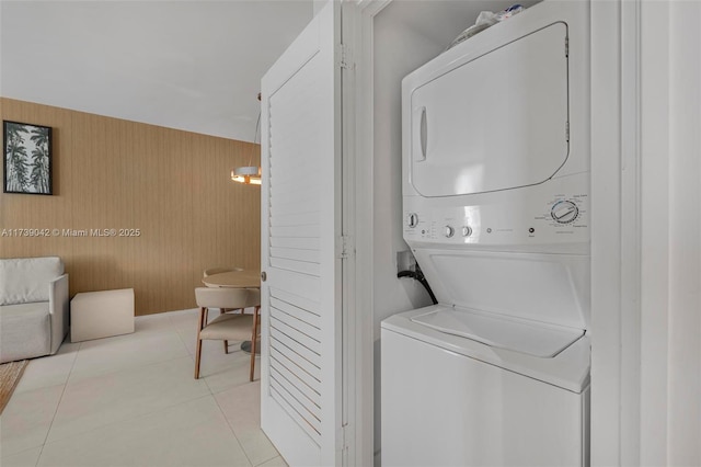 clothes washing area with stacked washing maching and dryer, light tile patterned floors, and wood walls