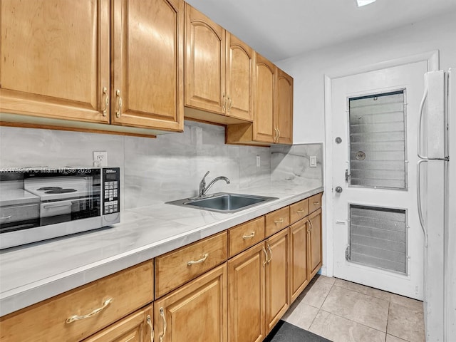 kitchen with light tile patterned floors, a sink, light countertops, backsplash, and freestanding refrigerator