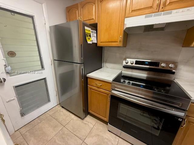 kitchen featuring brown cabinets, light tile patterned floors, stainless steel appliances, light countertops, and under cabinet range hood