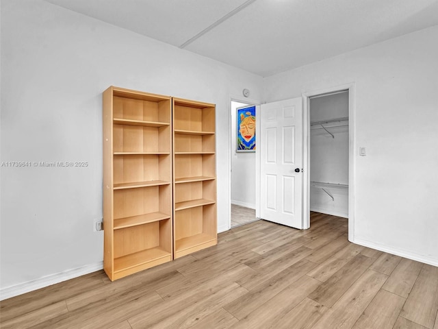 unfurnished bedroom featuring a walk in closet, a closet, light wood-style flooring, and baseboards