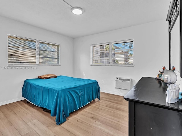 bedroom with light wood-type flooring, baseboards, and a wall mounted AC