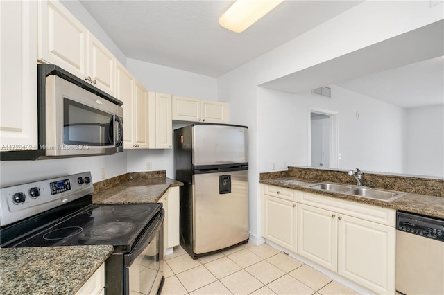 kitchen featuring appliances with stainless steel finishes, sink, dark stone counters, and light tile patterned floors