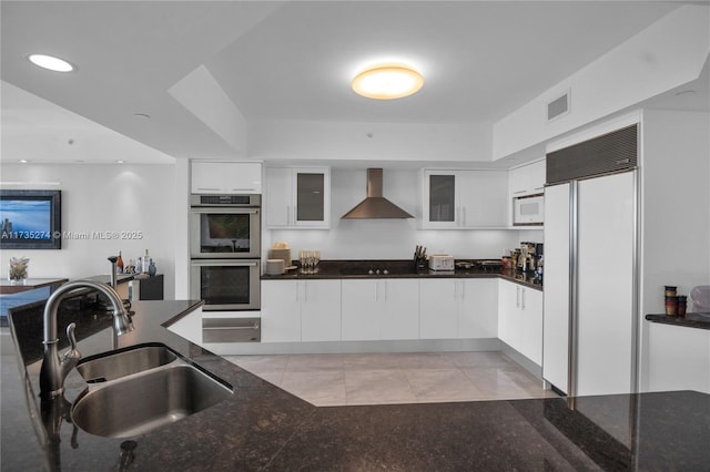 kitchen featuring sink, white cabinets, paneled refrigerator, stainless steel double oven, and wall chimney exhaust hood