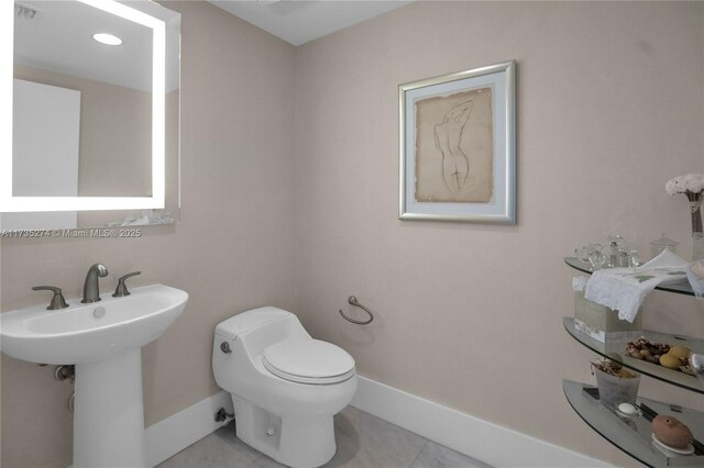 half bathroom featuring tile patterned floors, a sink, toilet, and baseboards