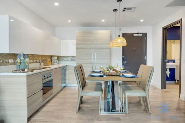 kitchen featuring light hardwood / wood-style flooring, appliances with stainless steel finishes, hanging light fixtures, backsplash, and white cabinets