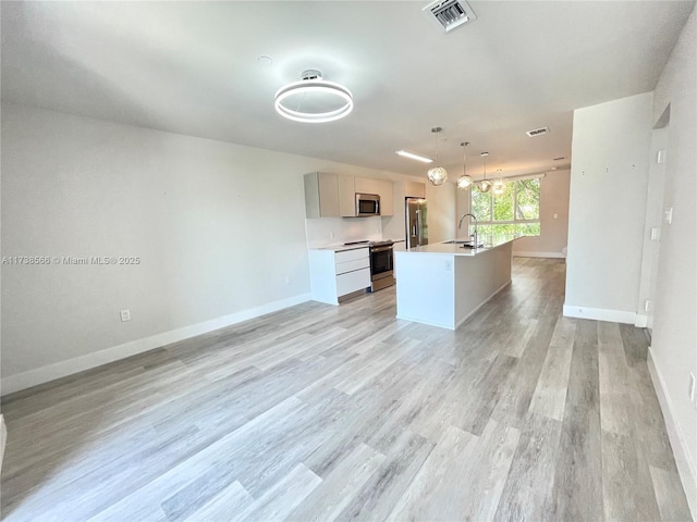 kitchen with sink, light hardwood / wood-style flooring, appliances with stainless steel finishes, a kitchen island with sink, and decorative light fixtures